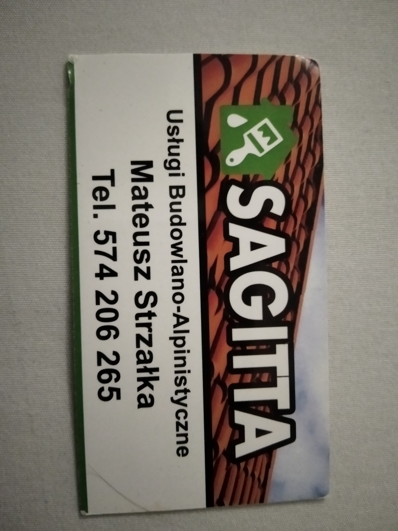 Wizytówka firmy Sagitta oferującej usługi budowlano-alpinistyczne, z ikoną pędzla i kropli farby, obok imienia i nazwiska Mateusza Strzałki oraz numeru telefonu.