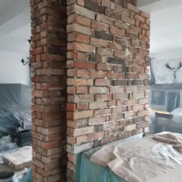 Kolumna wykończona starą cegłą w Jeleniej Górze, z widocznymi nierównościami i spoinami, tworząca rustykalny element dekoracyjny wnętrza w trakcie prac remontowych.