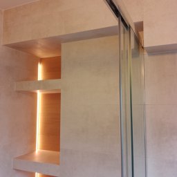 jaroslaw warakomski - Beżowa łazienka z kabiną prysznicową i podświetlanymi półkami wnękowymi. Minimalistyczny design, jasne płytki, szklane drzwi kabiny.