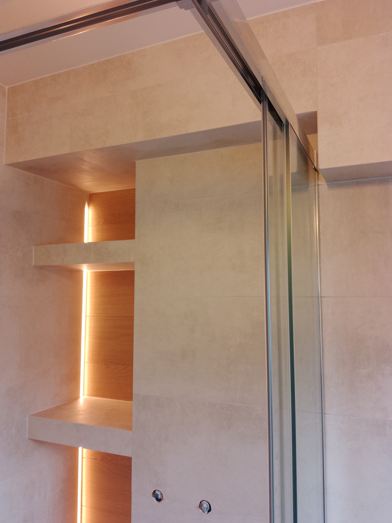 Beżowa łazienka z kabiną prysznicową i podświetlanymi półkami wnękowymi. Minimalistyczny design, płytki imitujące kamień, nowoczesne oświetlenie.