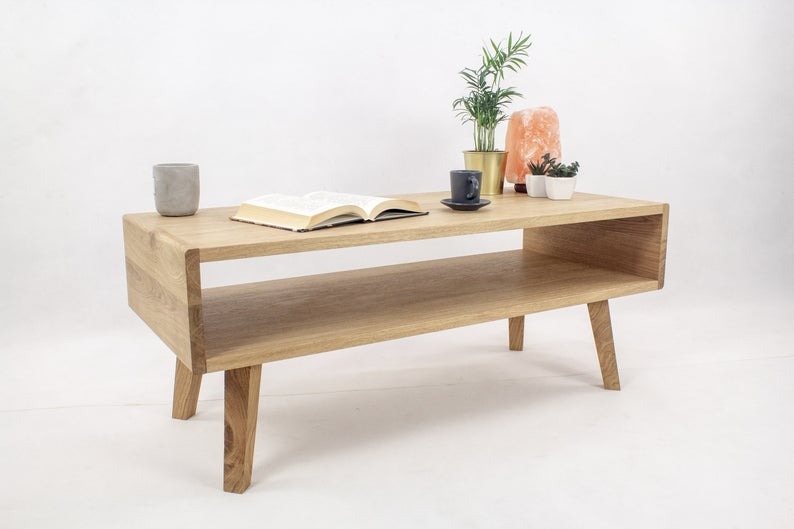 Drewniany stolik kawowy z półką, wykonany na zamówienie w Warszawie, z książką, filiżanką i roślinami na blacie, na białym tle.