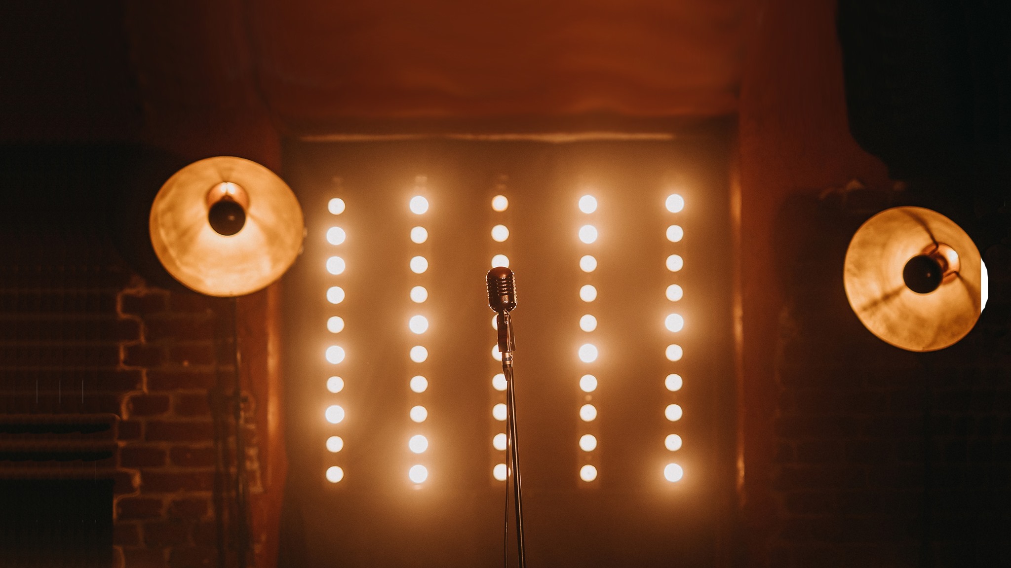 Vintage mikrofon na tle ściany z rzędami żarówek i lampami w stylu industrialnym po bokach, ceglana ściana w tle.