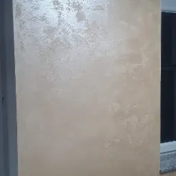 Ściana wewnętrzna z dekoracyjnym, beżowo-złotym efektem malowania, widoczna obok białej ramy drzwi i fragmentu parapetu okiennego.