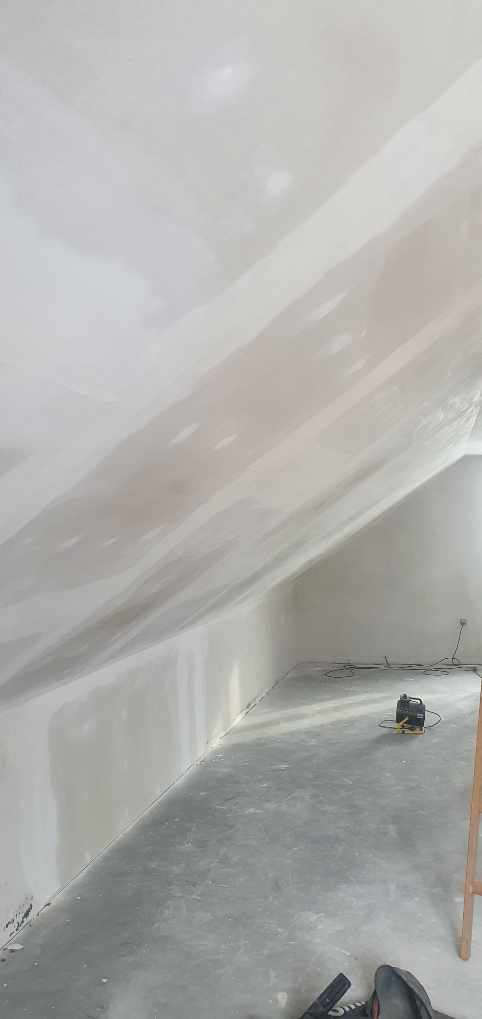 Poddasze ze skośnym sufitem po nałożeniu gładzi szpachlowej, widoczny wentylator budowlany do osuszania i fragment drabiny.