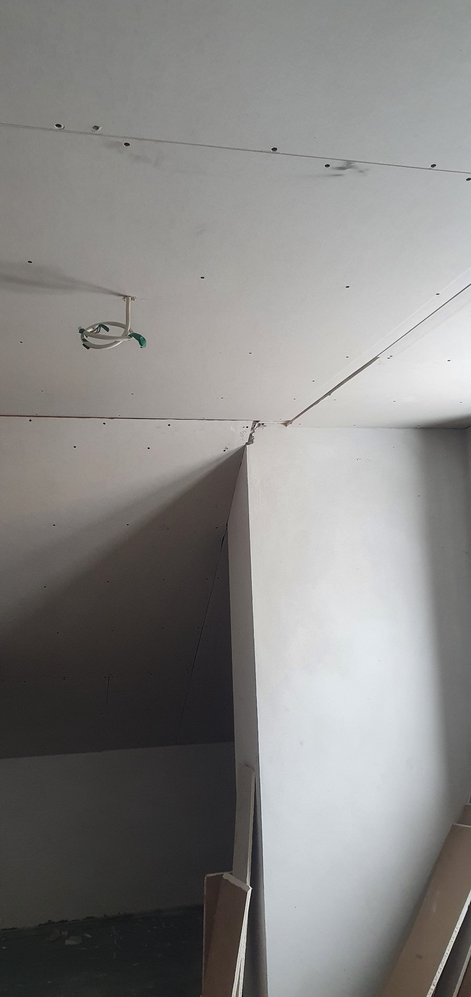 Montaż płyt karton-gips na suficie i ścianach, widoczne łączenia płyt, wystające przewody elektryczne i niedoskonałości w narożniku.