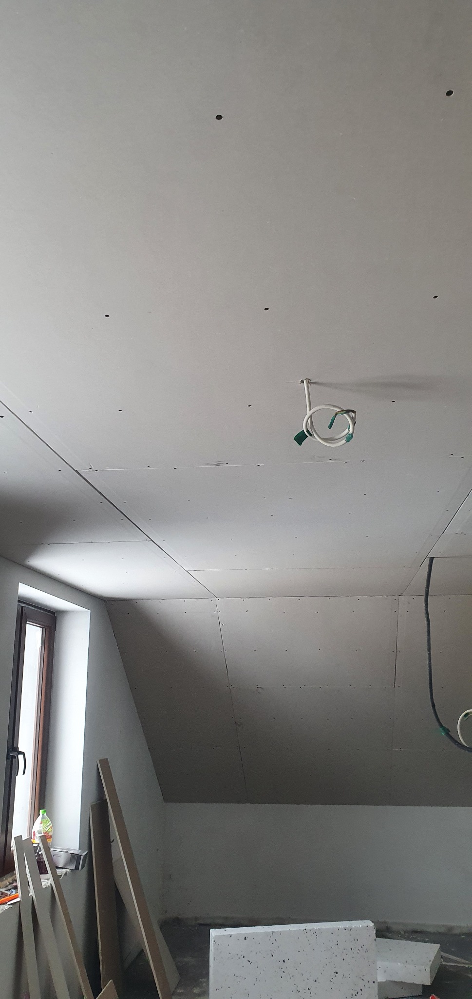Poddasze w trakcie wykańczania płytami kartonowo-gipsowymi, widoczne łączenia płyt, otwory po wkrętach i wystające przewody elektryczne.