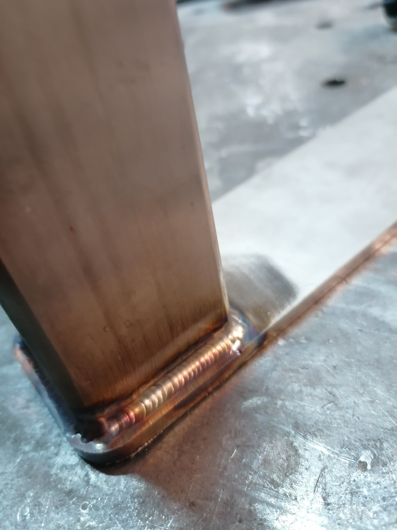 Spoina spawalnicza łącząca pionowy profil ze stalową płytą, widoczne ślady obróbki na powierzchni metalu.