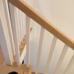 Widok z góry na fragment montowanych schodów: drewniane stopnie i białe balustrady, widoczny silikon i czarna szmatka.