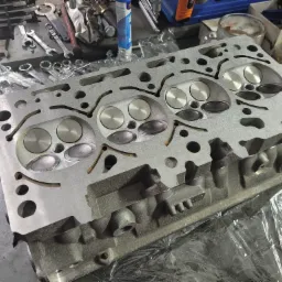 Zdemontowana głowica silnika 2.0 TFSI na warsztatowym stole, widoczne zawory i kanały, obok narzędzia i preparaty.