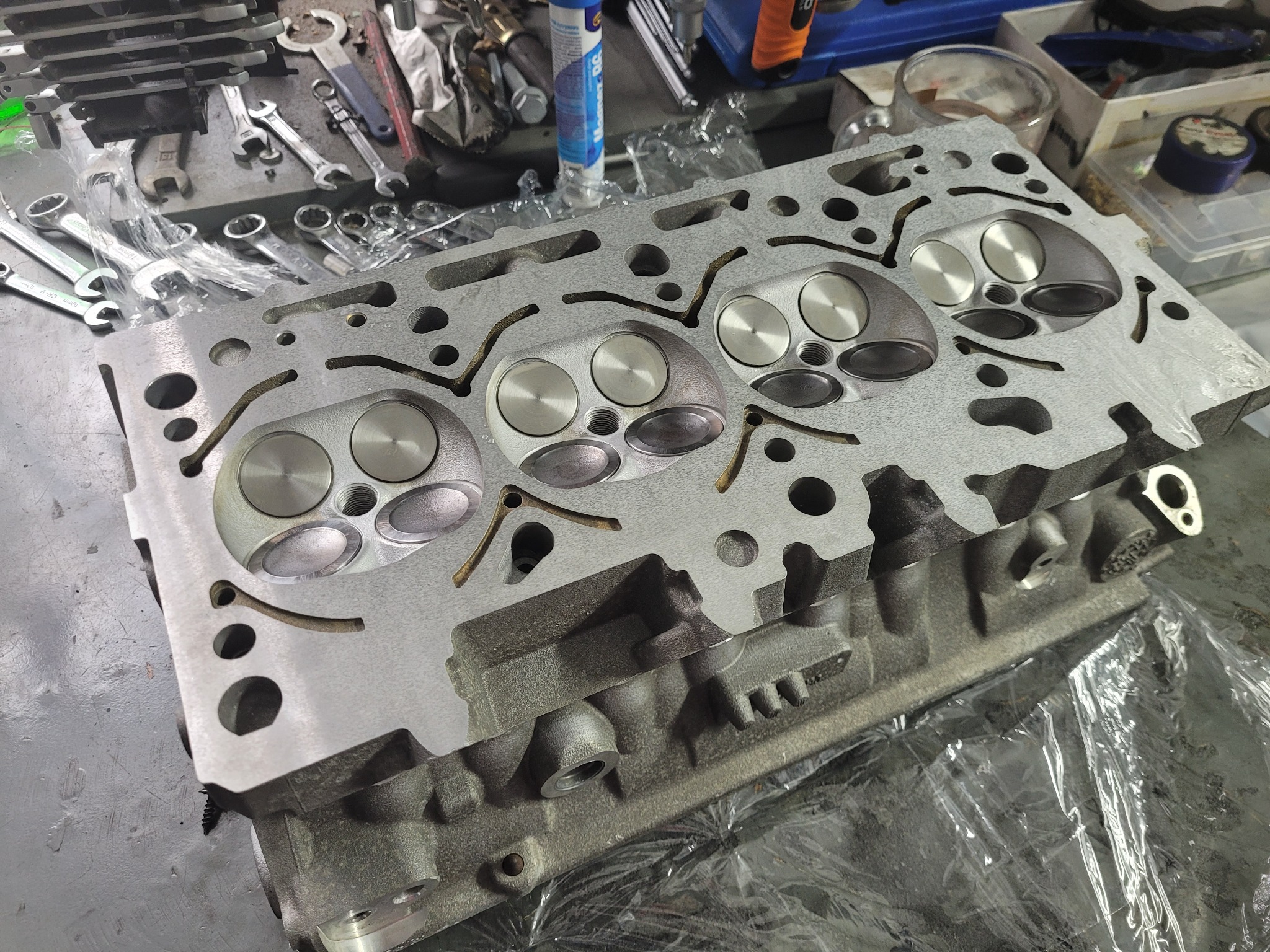 Zdemontowana głowica silnika 2.0 TFSI na warsztatowym stole, widoczne zawory i kanały, obok narzędzia i preparaty.