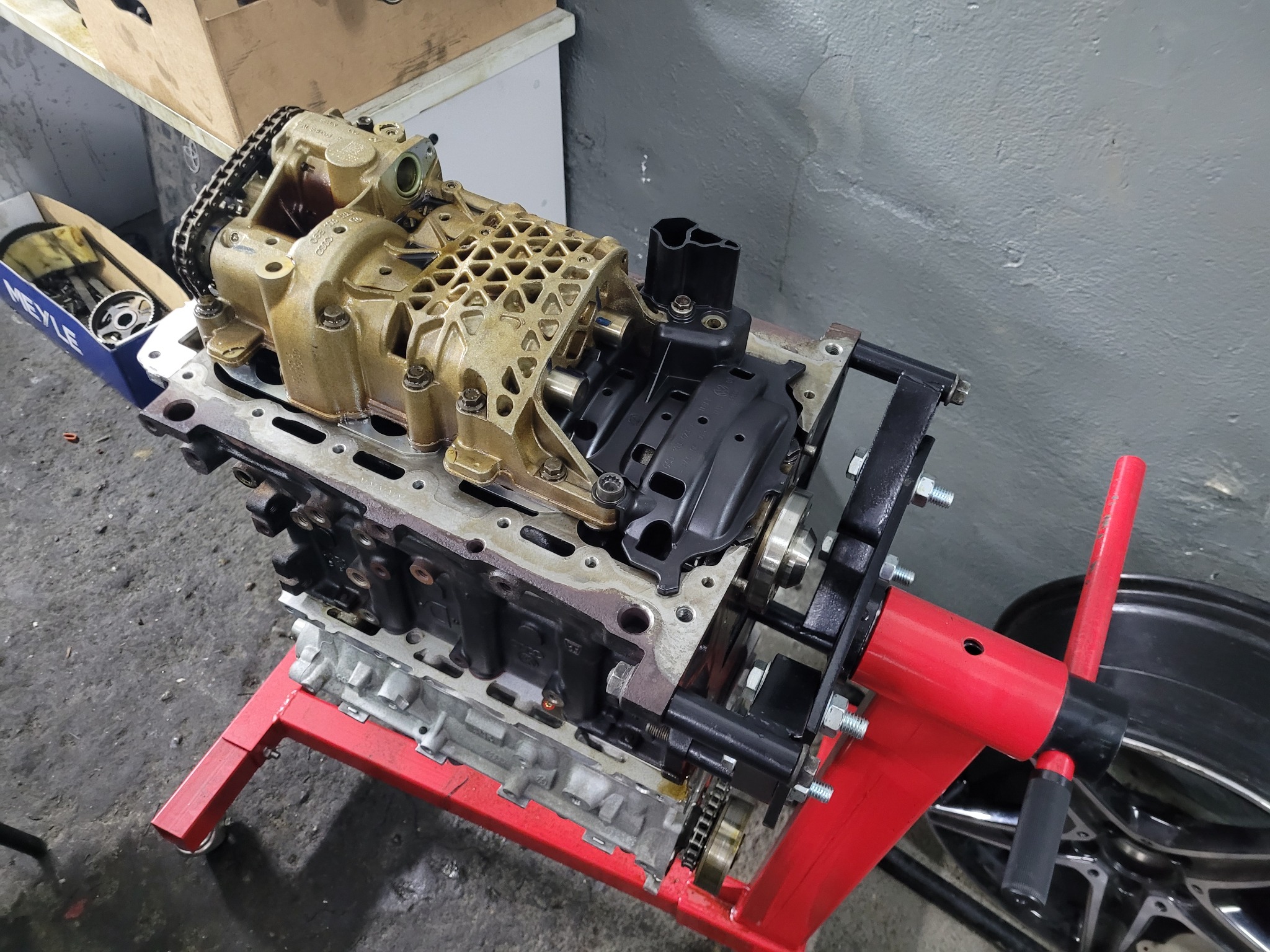 Zdemontowany silnik 2.0 TFSI na czerwonym stojaku warsztatowym, widoczna pompa oleju z łańcuchem i skrzynia korbowa.