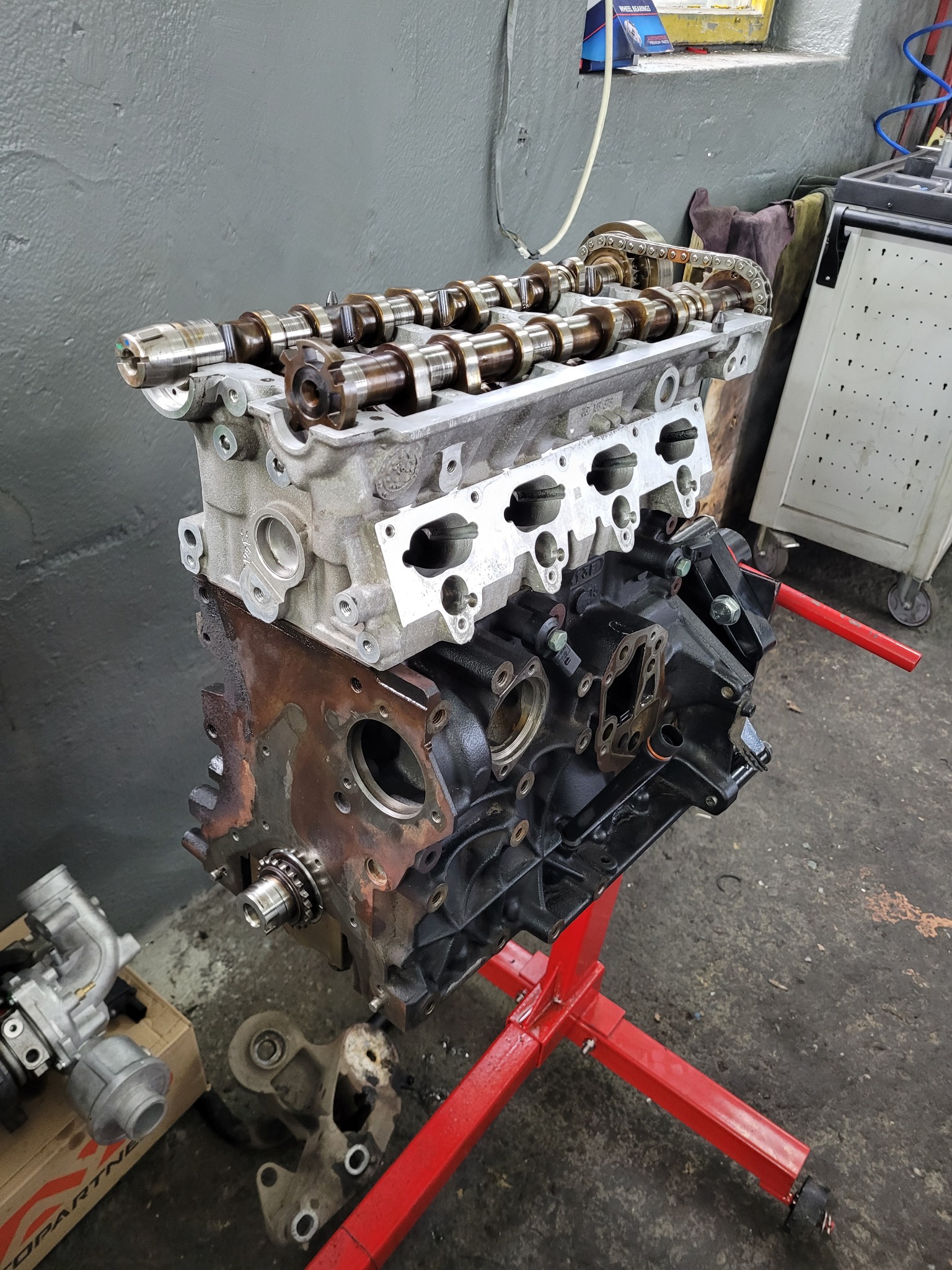 Zdemontowany silnik 2.0 TFSI na czerwonym stojaku warsztatowym, widoczne wałki rozrządu, łańcuch rozrządu, blok silnika, turbosprężarka obok