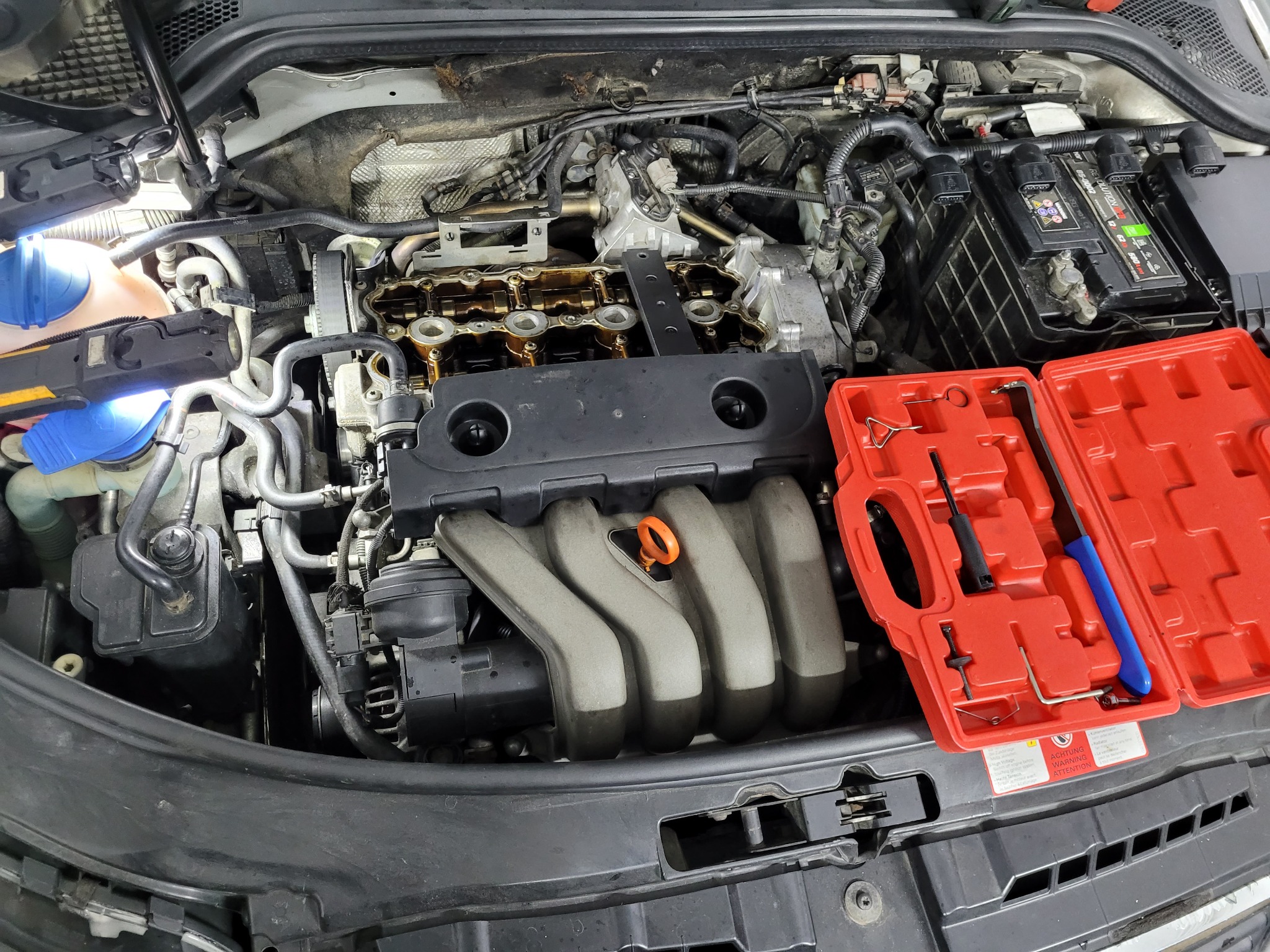 Otwarty silnik 2.0 FSI w trakcie naprawy, widoczna głowica, kolektor dolotowy i zestaw narzędzi w czerwonym pudełku, oświetlony lampą warsztatową.
