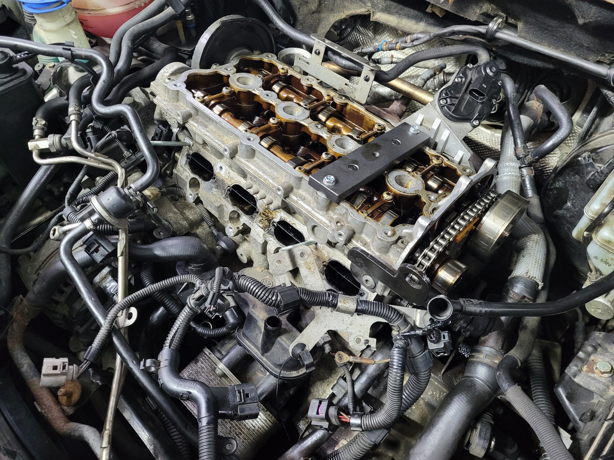 Otwarty silnik samochodowy z widocznymi wałkami rozrządu i łańcuchem, zabezpieczony metalową płytką, w trakcie serwisu.