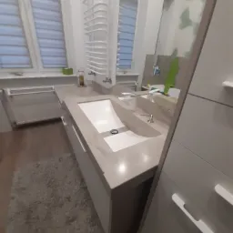 Łazienka z umywalką wpuszczoną w beżowy blat, widoczna grzejnik drabinkowy i fragment szafy.