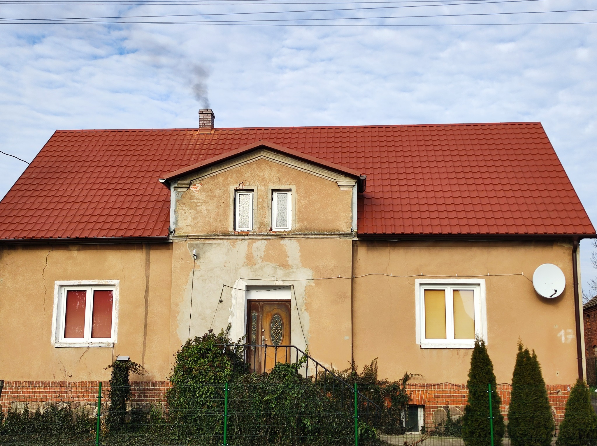 Dom w Rawiczu z nowym, czerwonym dachem z dachówki ceramicznej, komin z cegły, z którego unosi się dym.