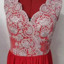 Czerwona suknia wieczorowa z koronkową górą na czerwonym manekinie, delikatne zdobienia z cekinów.