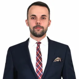 Portret mężczyzny w granatowym garniturze, białej koszuli i krawacie w czerwoną i niebieską kratę, z ozdobną poszetką w kieszonce.