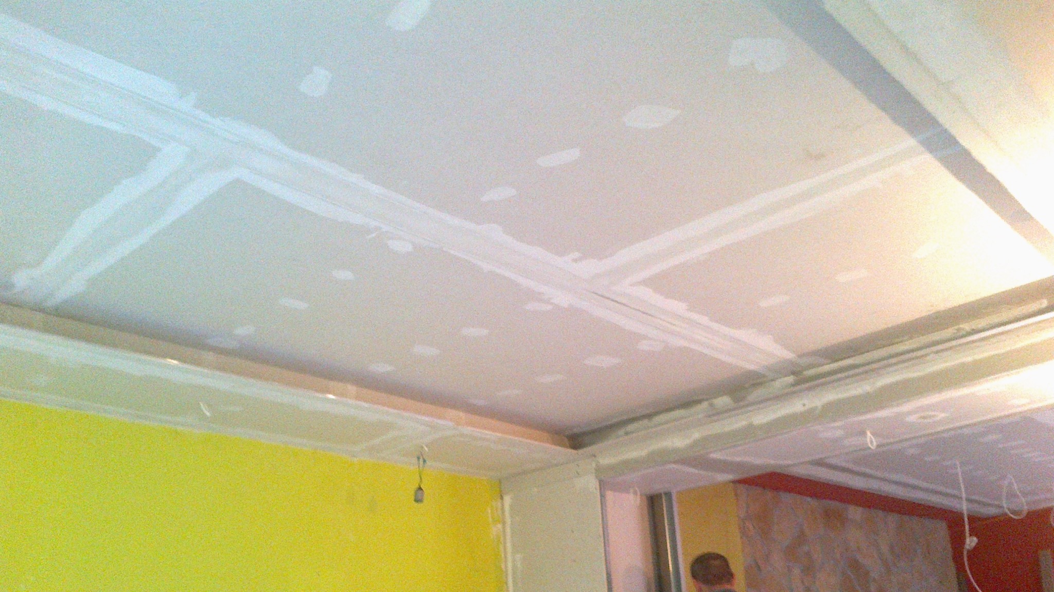 Sufit podwieszany z płyt kartonowo-gipsowych w trakcie szpachlowania łączeń, widoczna żółta ściana w tle i fragment instalacji elektrycznej.