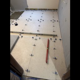 Skanbud - Układanie jasnych płytek podłogowych z użyciem poziomicy i klipsów. Częściowo położone płytki z klejem w tle. Remont w trakcie.