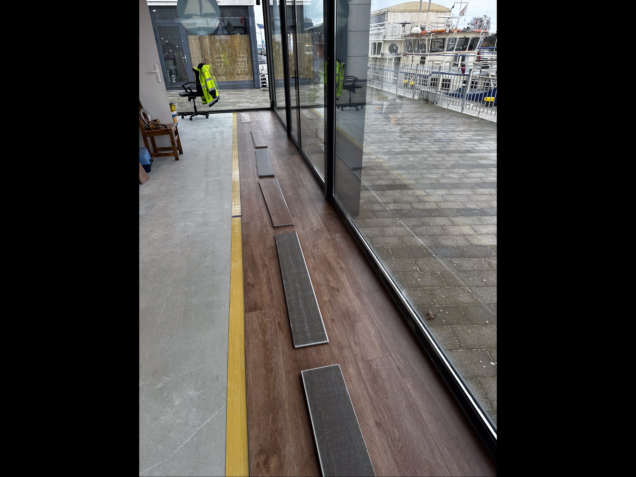 Układanie paneli podłogowych w Szczecinie, widok z góry. Panele w odcieniach brązu ułożone częściowo, z widokiem na przeszkloną ścianę i nabrzeże.