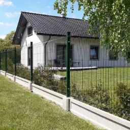 Zielone panele ogrodzeniowe na betonowej podmurówce otaczające posesję z białym domem i zadbanym trawnikiem.