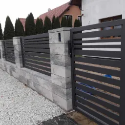 Nowoczesna brama wjazdowa i przęsła ogrodzeniowe z poziomych, szarych profili, osadzone na betonowych słupkach i podmurówce z szarej kostki, na tle domu z czerwonym dachem i tujami.