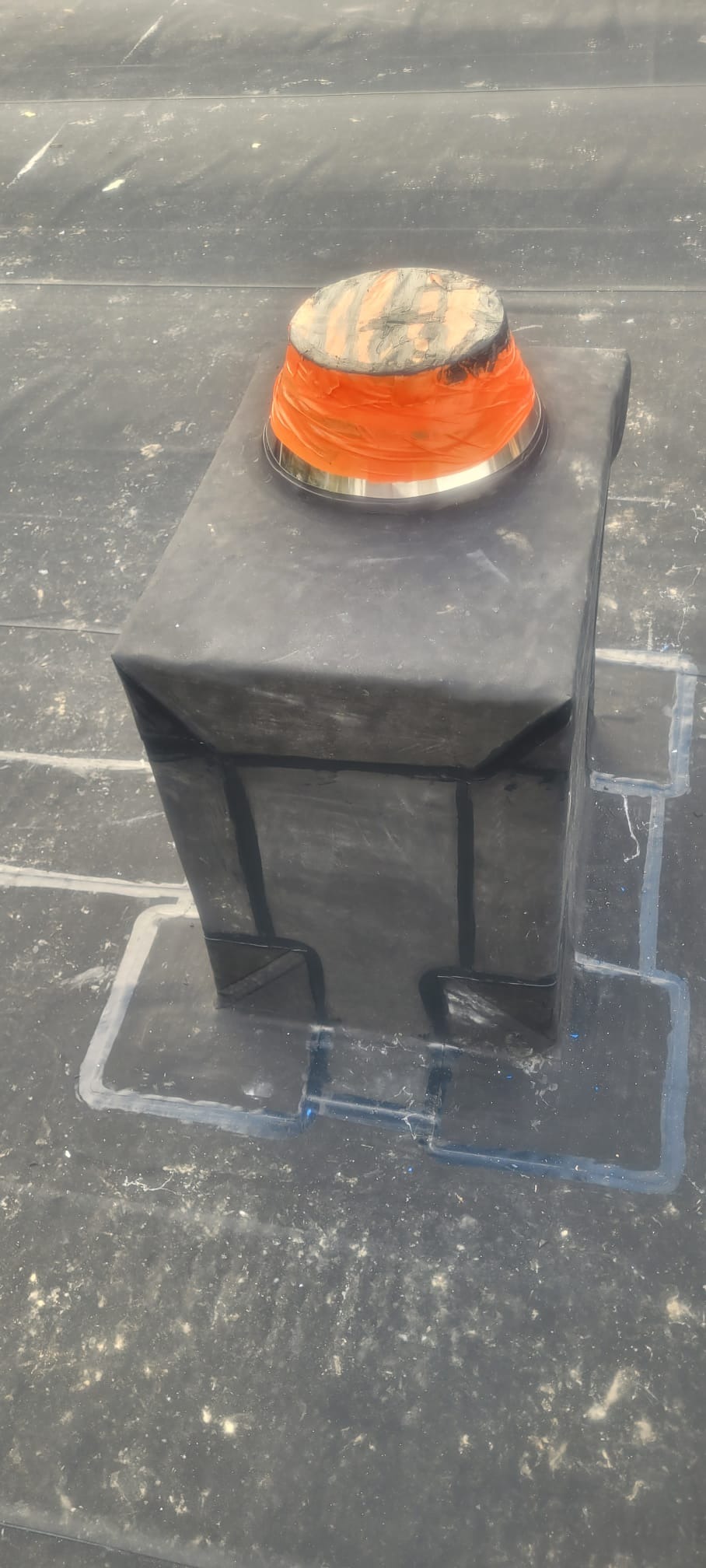 Szczegółowo zabezpieczony komin na dachu pokrytym papą, z widocznymi uszczelnieniami i elementami wykończeniowymi. Praca dekarska z bliska.