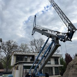 PM-BAU Budownictwo Energooszczędne - Budowa domu z betonu komórkowego w toku, widoczny dźwig budowlany i pracownik. Elementy konstrukcyjne, okna wstawione, tło: pochmurne niebo.
