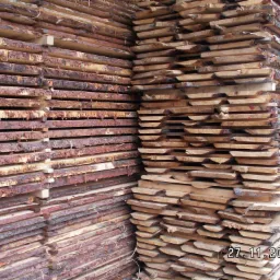 Stosy świeżo przetartej tarcicy sosnowej z korą, ułożone warstwami, widoczne przekładki między warstwami, data 27.11.2006 w prawym dolnym rogu.