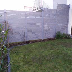 PolixBud - Szare, poziome ogrodzenie panelowe z drewnianych listew, oddzielające trawnik od posesji sąsiada, z widocznym fragmentem domu z balkonem i oknem z roletami.