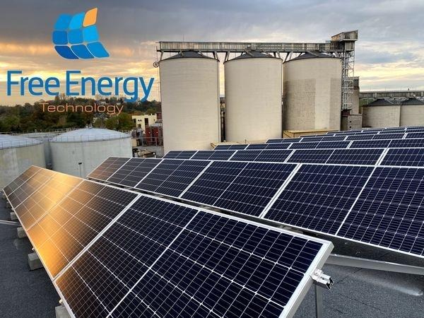 Instalacja paneli słonecznych na dachu przemysłowym z widocznymi silosami w tle, logo firmy Free Energy Technology w lewym górnym rogu.