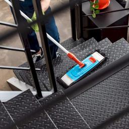 BlueService Sp. z o.o. - Osoba w zielonych rękawicach czyści metalowe schody mopem z niebieską nakładką, widoczne czarne poręcze i dekoracyjny stolik z rośliną w tle.