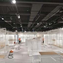 BlueService Sp. z o.o. - Wnętrze sklepu w trakcie porządkowania, widoczny pracownik w pomarańczowej kamizelce i odkurzacz przemysłowy na błyszczącej podłodze, oświetlenie szynowe na suficie.