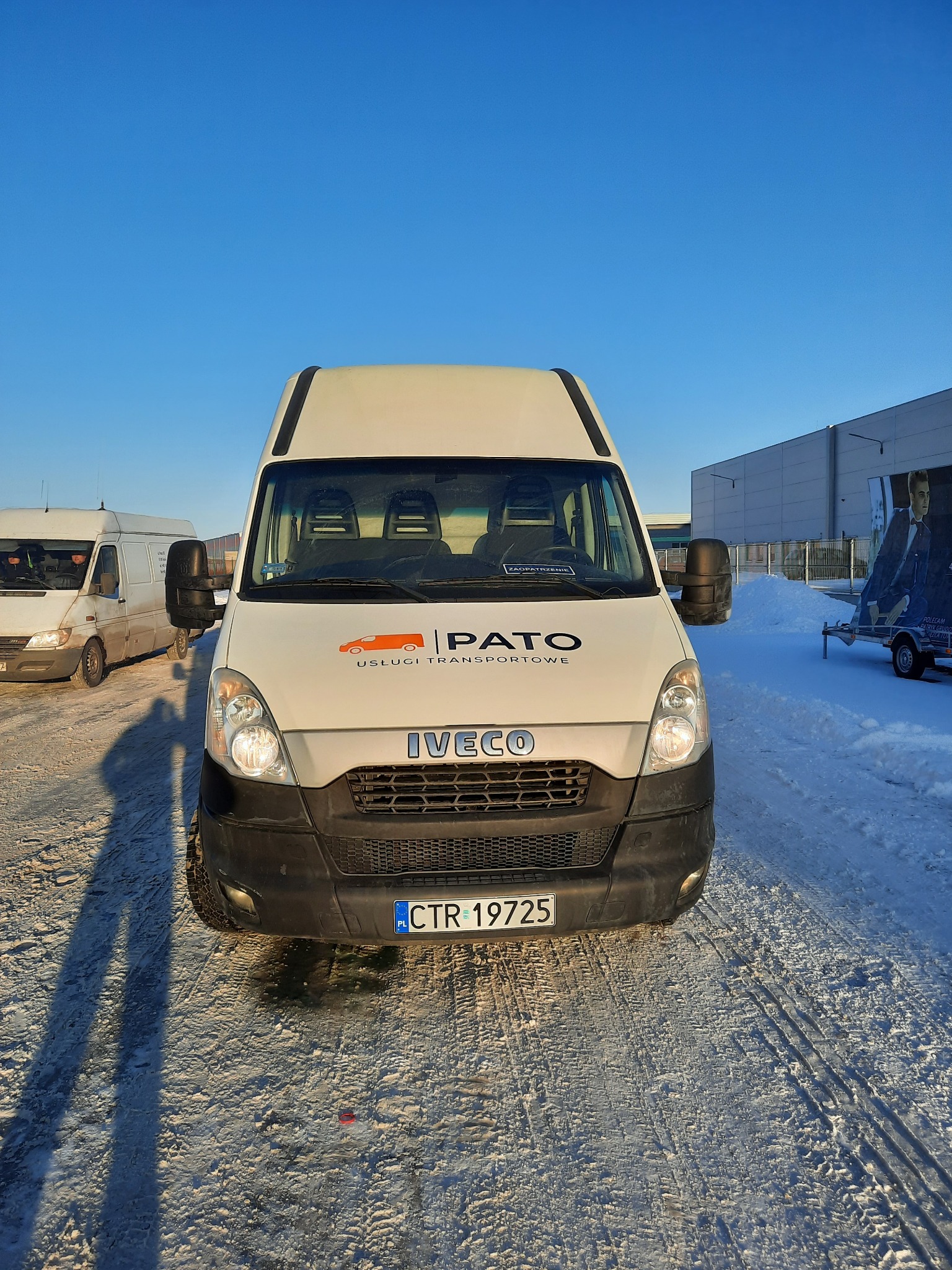 Biały bus Iveco z logo firmy transportowej PATO na tle zimowego krajobrazu i błękitnego nieba. Widoczny numer rejestracyjny CTR 19725.