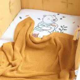 Żółty kocyk z dzianiny w dziecięcym łóżeczku z motywem misia trzymającego miód na poduszce.