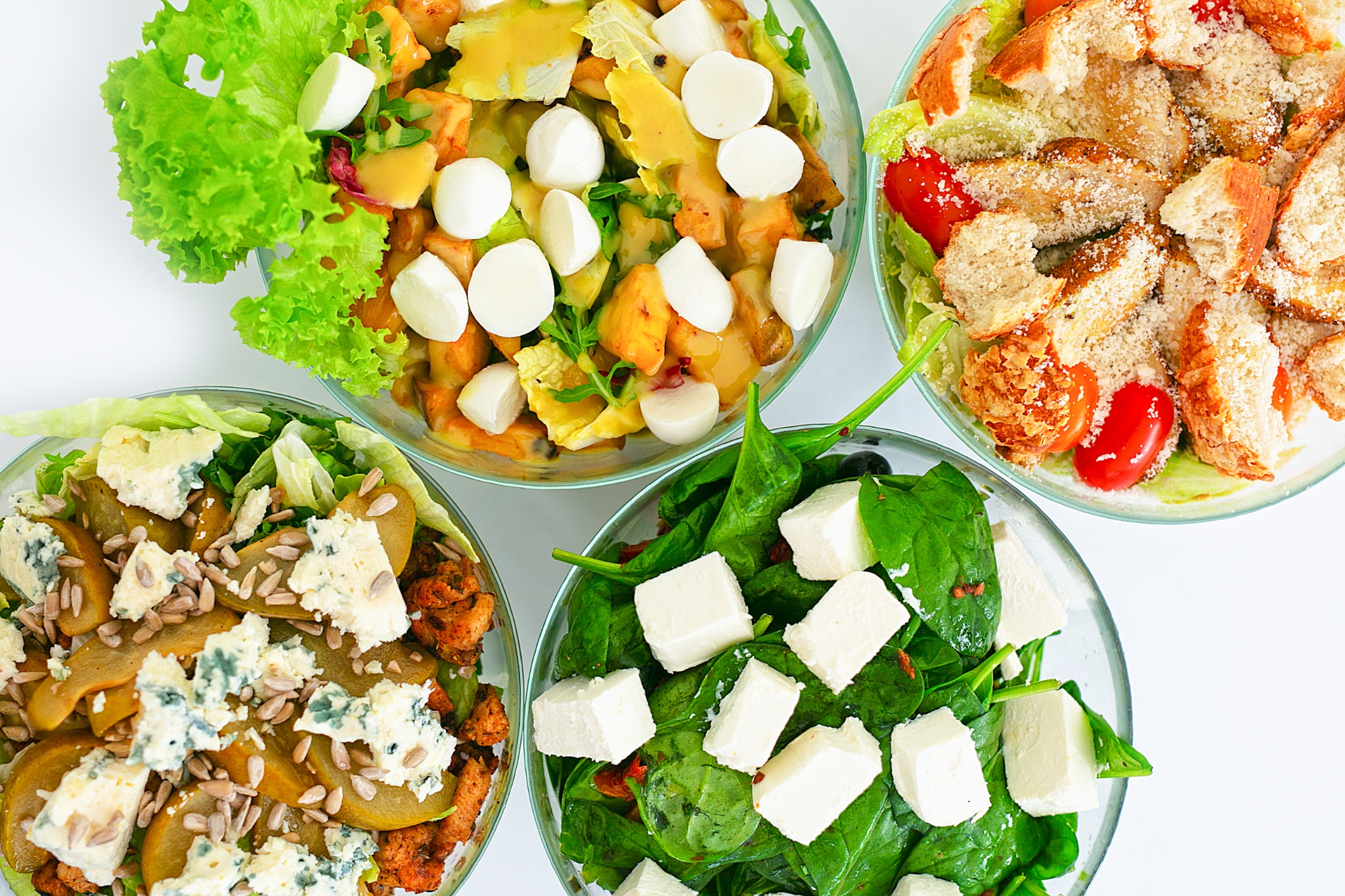 Cztery szklane miski z różnymi rodzajami sałatek: z grillowanym kurczakiem, gruszką i serem pleśniowym, z pomidorami, grzankami i parmezanem, z mozzarellą i sosem musztardowym oraz ze szpinakiem...