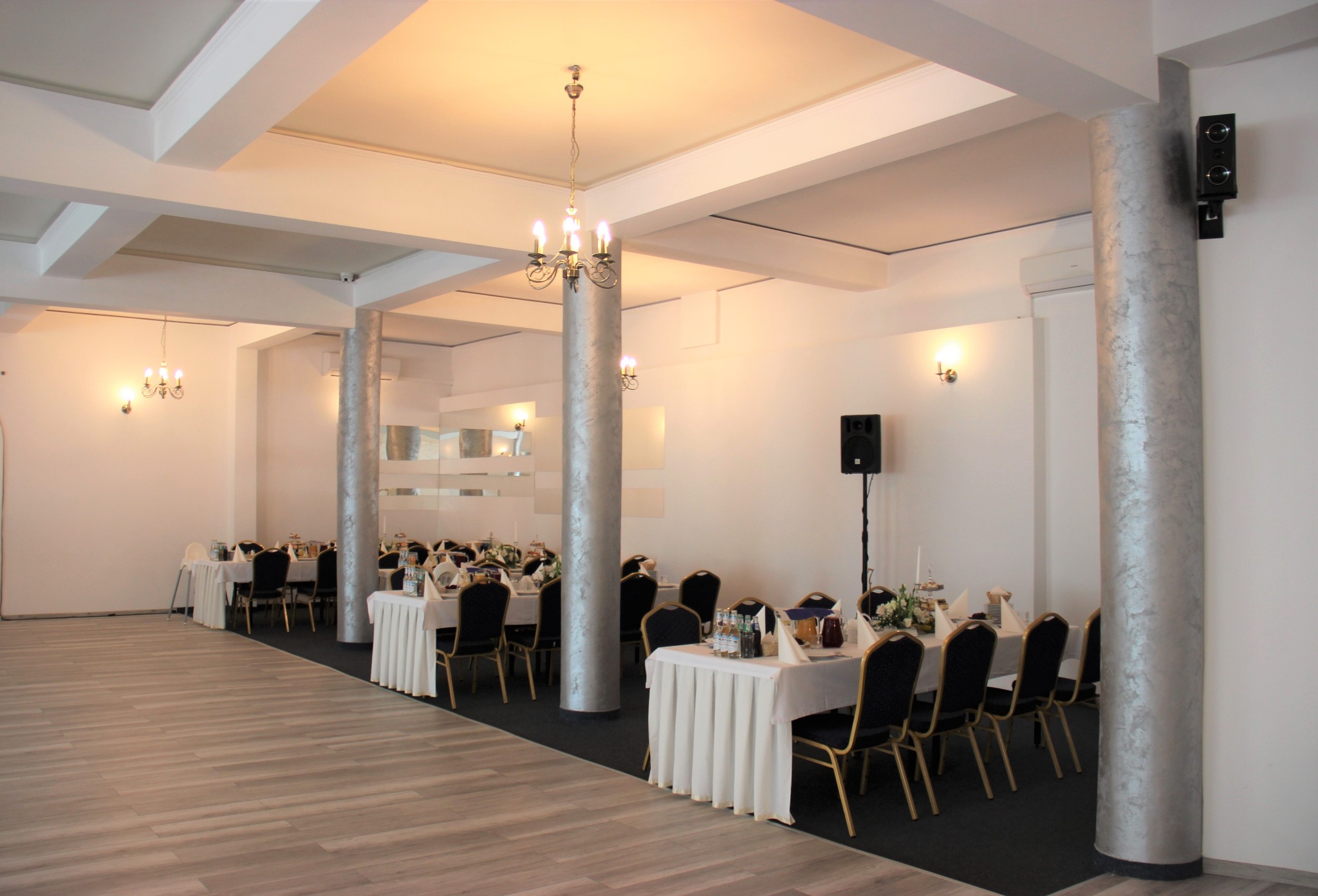 Sala bankietowa z nakrytymi stołami, srebrne kolumny dekoracyjne, parkiet w odcieniach beżu i szarości.