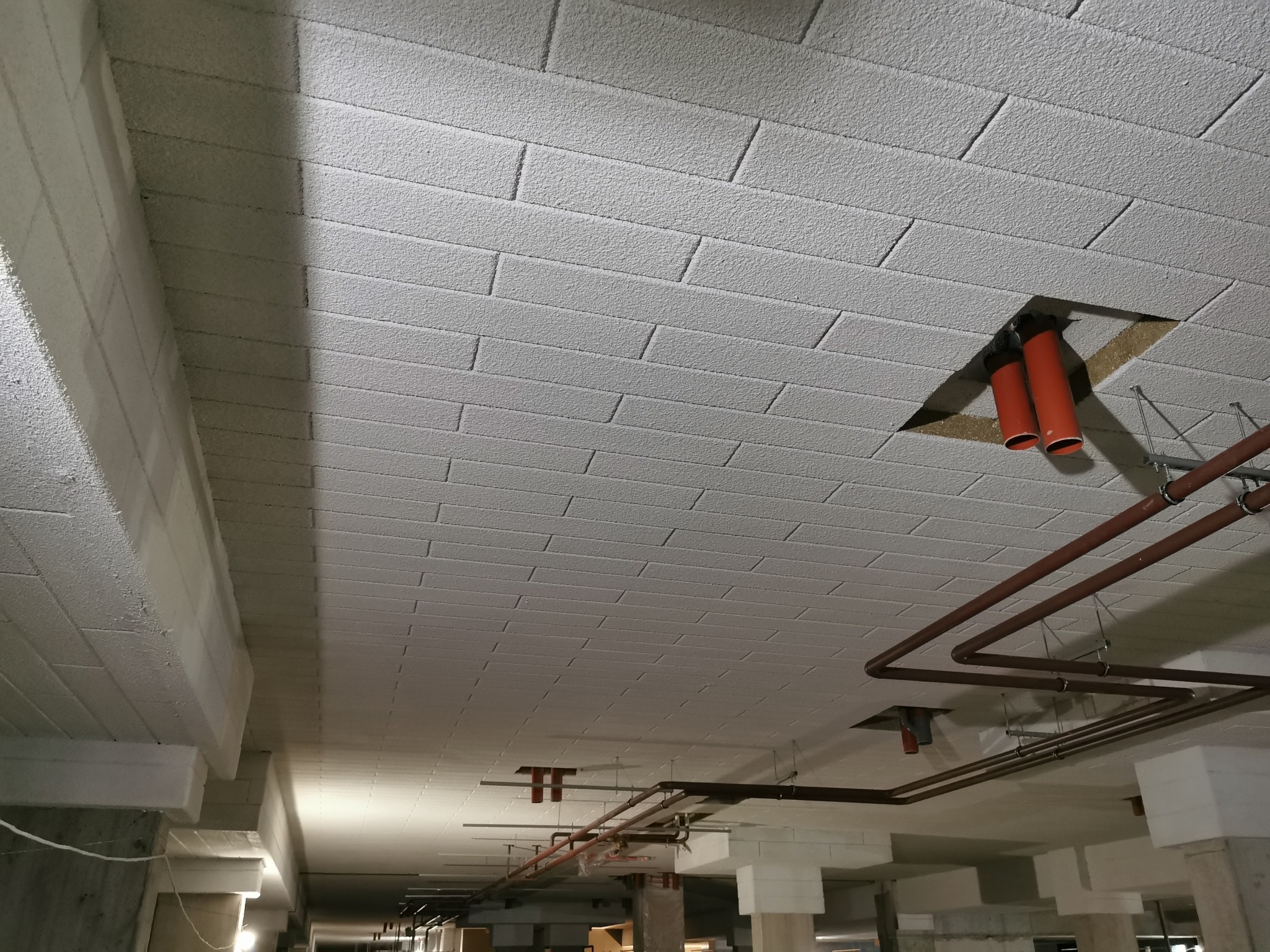 Poddasze po natrysku izolacji piankowej, widoczne rury instalacyjne i fragmenty konstrukcji budynku.