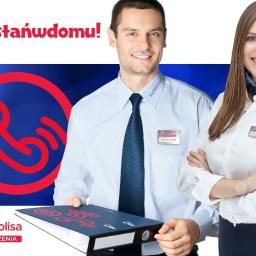 Biljer Małgorzata Bilowicka - Uśmiechnięci konsultanci firmy ubezpieczeniowej z identyfikatorami na tle firmowego logo i hasła #zostańwdomu, mężczyzna trzyma segregator.