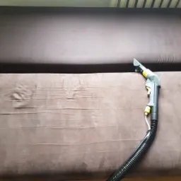 Dysza odkurzacza piorącego na brązowej kanapie podczas czyszczenia, widoczne ślady wilgoci na tapicerce.