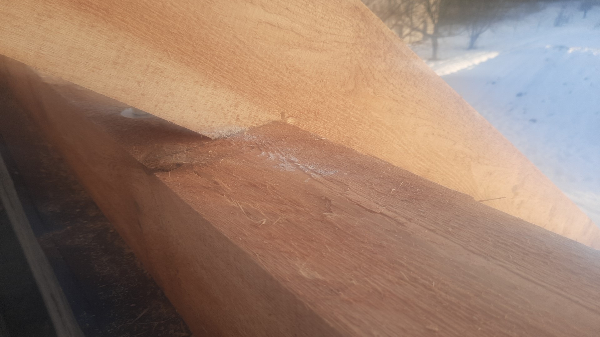 Fragment drewnianej konstrukcji dachu w trakcie montażu, widoczne połączenie belek na tle zaśnieżonego krajobrazu.