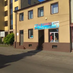 Fasada budynku z szyldem 'Auto Części Serwis', widok z ulicy w słoneczny dzień.