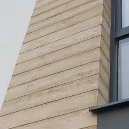 Fragment elewacji budynku z drewnopodobną okładziną ułożoną poziomo, przylegającą do białego tynku strukturalnego i szarej ramy okiennej.