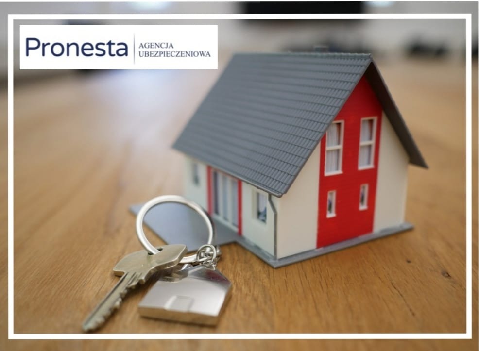 Mały model domu z czerwonym akcentem na drewnianym stole, z kluczami na pierwszym planie, logo agencji ubezpieczeniowej w lewym górnym rogu.