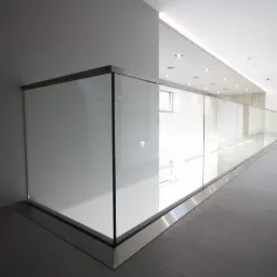 Długa szklana balustrada z metalowym wykończeniem w nowoczesnym wnętrzu, widok z dołu, jasne oświetlenie.