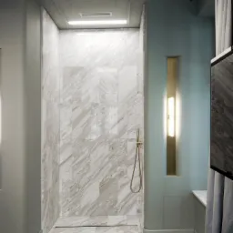 Nowoczesna kabina prysznicowa wyłożona płytami z jasnego marmuru o nieregularnym wzorze żyłkowania, z odpływem liniowym i złotą słuchawką prysznicową, oświetlona listwą LED.