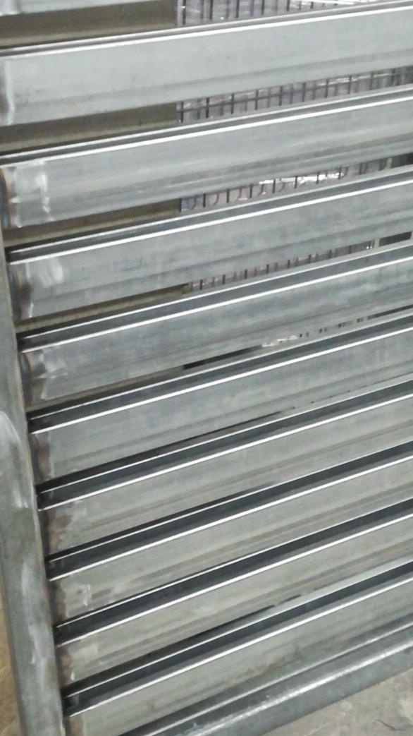 Szare, metalowe profile zamknięte ułożone równolegle, tworzące konstrukcję bramy lub ogrodzenia w trakcie spawania.