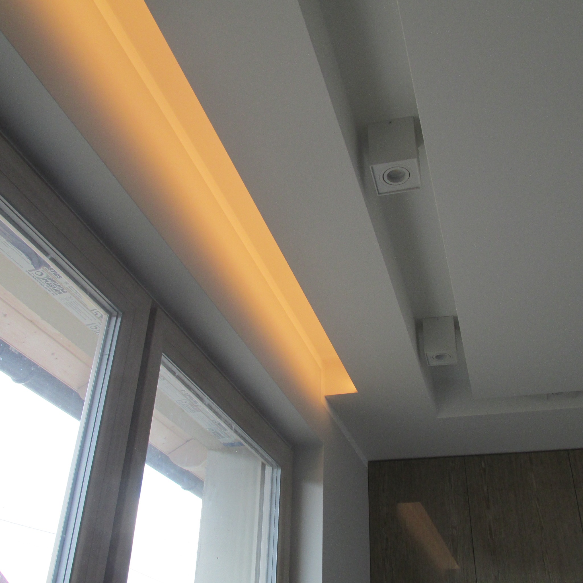 Sufit podwieszany z oświetleniem LED wzdłuż okna, widoczne także wbudowane reflektory punktowe i fragment szafki.