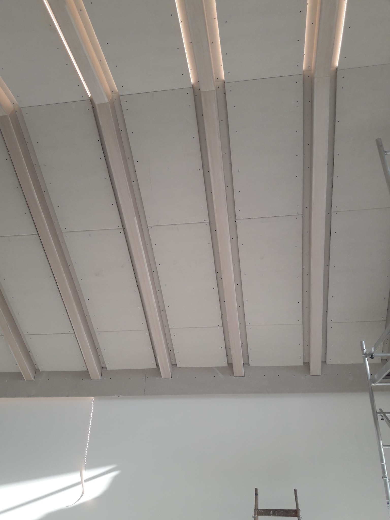 Sufit podwieszany z płyt gipsowo-kartonowych z widoczną konstrukcją nośną i ukrytym oświetleniem LED w szczelinach, widok z dołu podczas montażu.